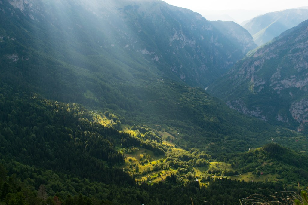 view of Durmitor national park from the trail to Curevac viewpoint with the sun piercing the clouds to illuminate the green forest